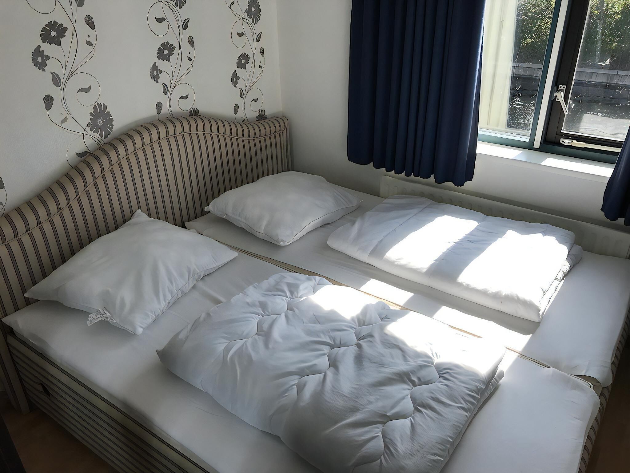 Een kamer met twee bedden, een gestreepte bank en een raam met gordijnen.