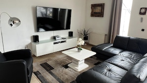 A modern living room with a flat-screen TV, black leather sofa, white entertainment unit, and a coffee table. - Park Brekkense Wiel 173 (Lemmer)