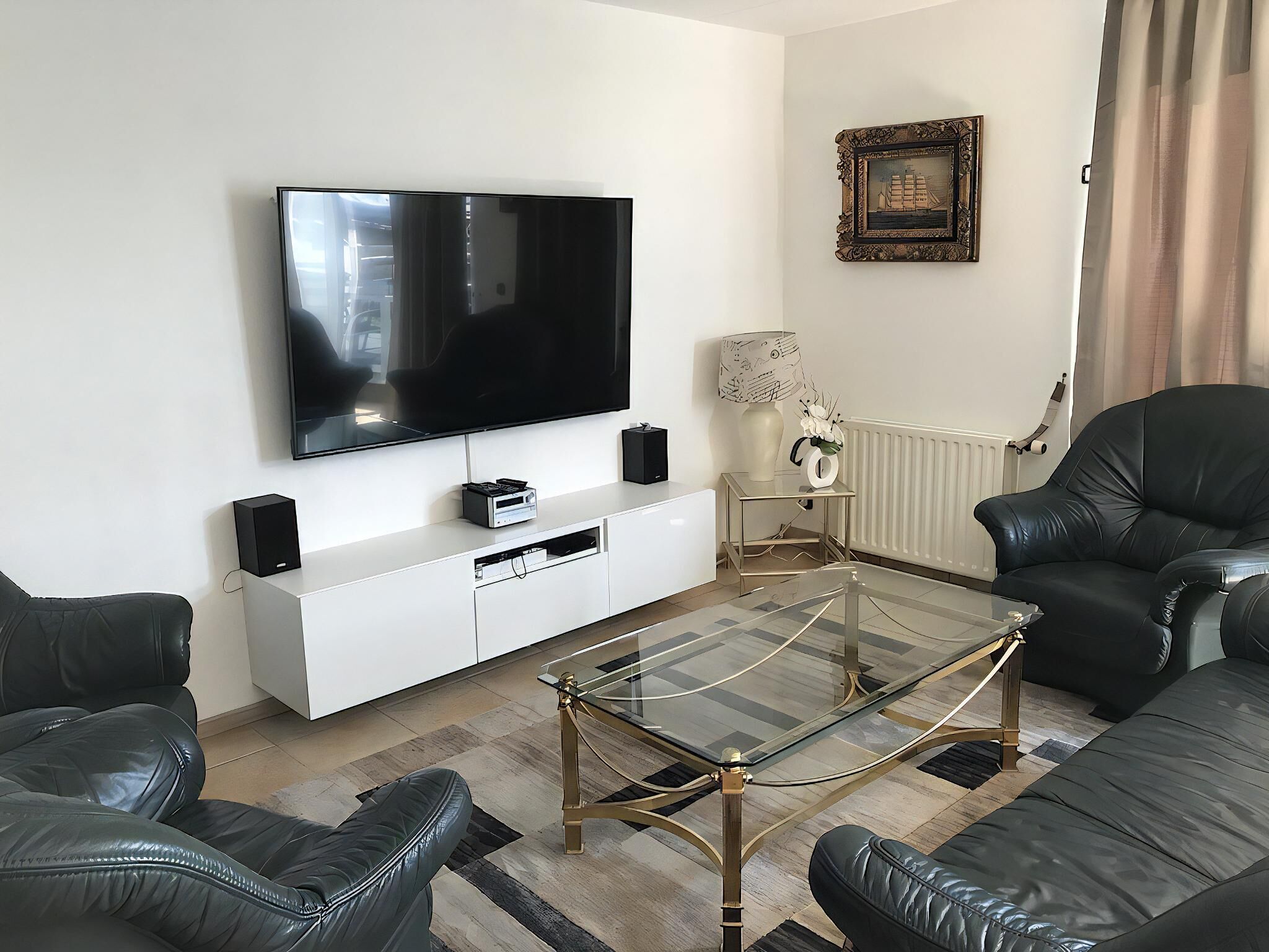 A modern living room with a flat-screen TV, leather sofas, a glass coffee table, and a white entertainment unit.
