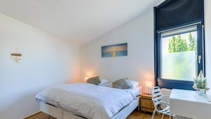A modern bedroom with a bed, bedside table, lamp, and a desk with a chair.