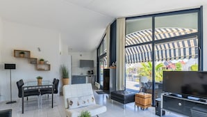 A modern living room with a large window, a flat-screen TV, and a dining area with a table and chairs.