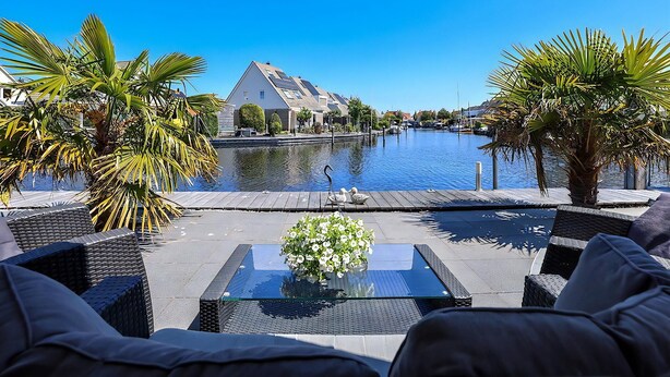 A waterfront patio with outdoor seating, a pool, and a view of a residential area.