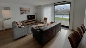 A modern living room with a grey sofa, a brown sofa, a TV on a wooden stand, and a dining area with chairs. - Park Brekkense Wiel 038 (Lemmer)