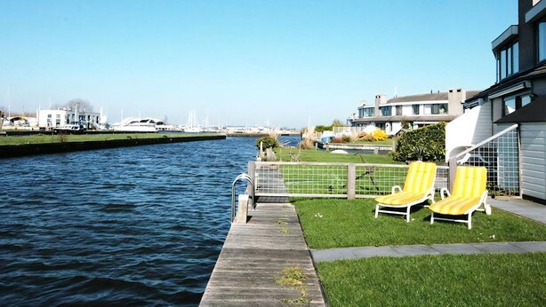 A waterfront property with a dock, two yellow lounge chairs, and a modern building with large windows. - Park Brekkense Wiel 038 (Lemmer)