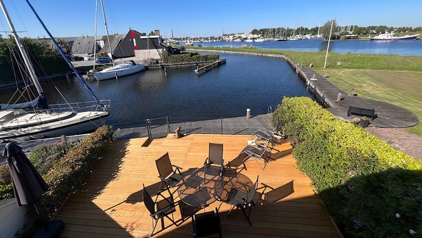 A marina with boats docked, a wooden deck with outdoor seating, and a clear view of the water. - Park Brekkense Wiel 229 (Lemmer)