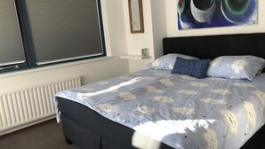 A bedroom with a bed, a window with blinds, a radiator, a framed picture, and a painting on the wall. - Park Brekkense Wiel 229 (Lemmer)