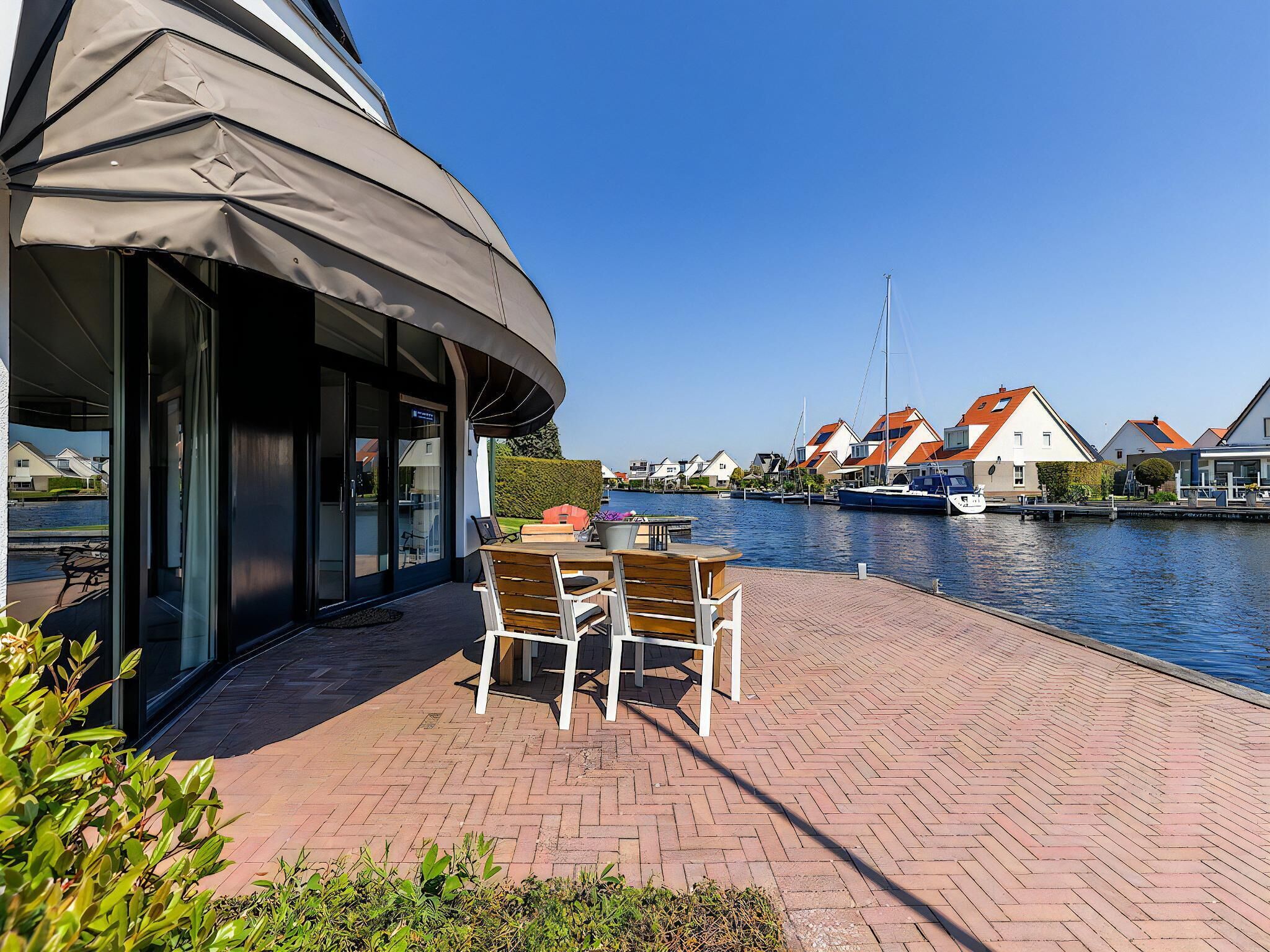 A waterfront patio with a table and chairs, a covered seating area, and a view of boats and houses across the water.