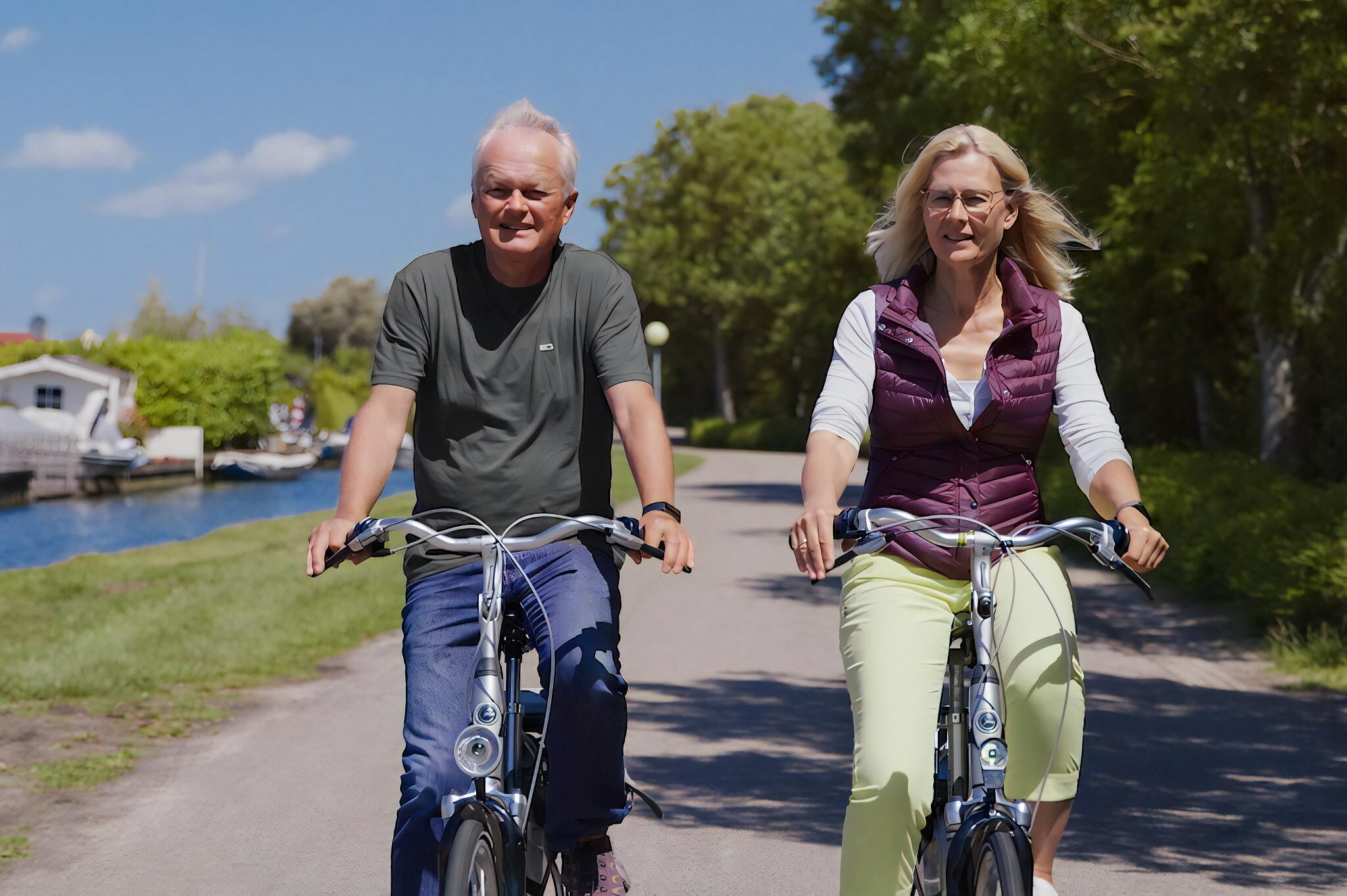 Twee personen fietsen op een verhard pad, met een waterpartij en groen in de achtergrond.
