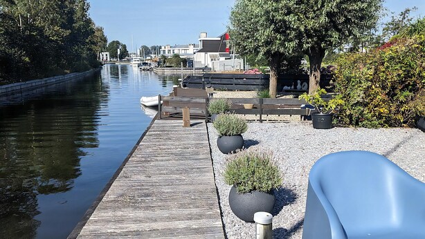 A wooden dock extending into calm water, surrounded by potted plants and a blue bench. - Park Brekkense Wiel 103 (Lemmer)
