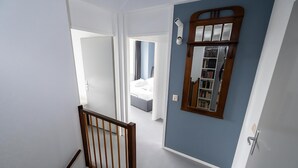 A hallway with a staircase leading to a bedroom. A wooden railing is visible on the left, and a mirror with a wooden frame is on the right wall. - Park Brekkense Wiel 103 (Lemmer)
