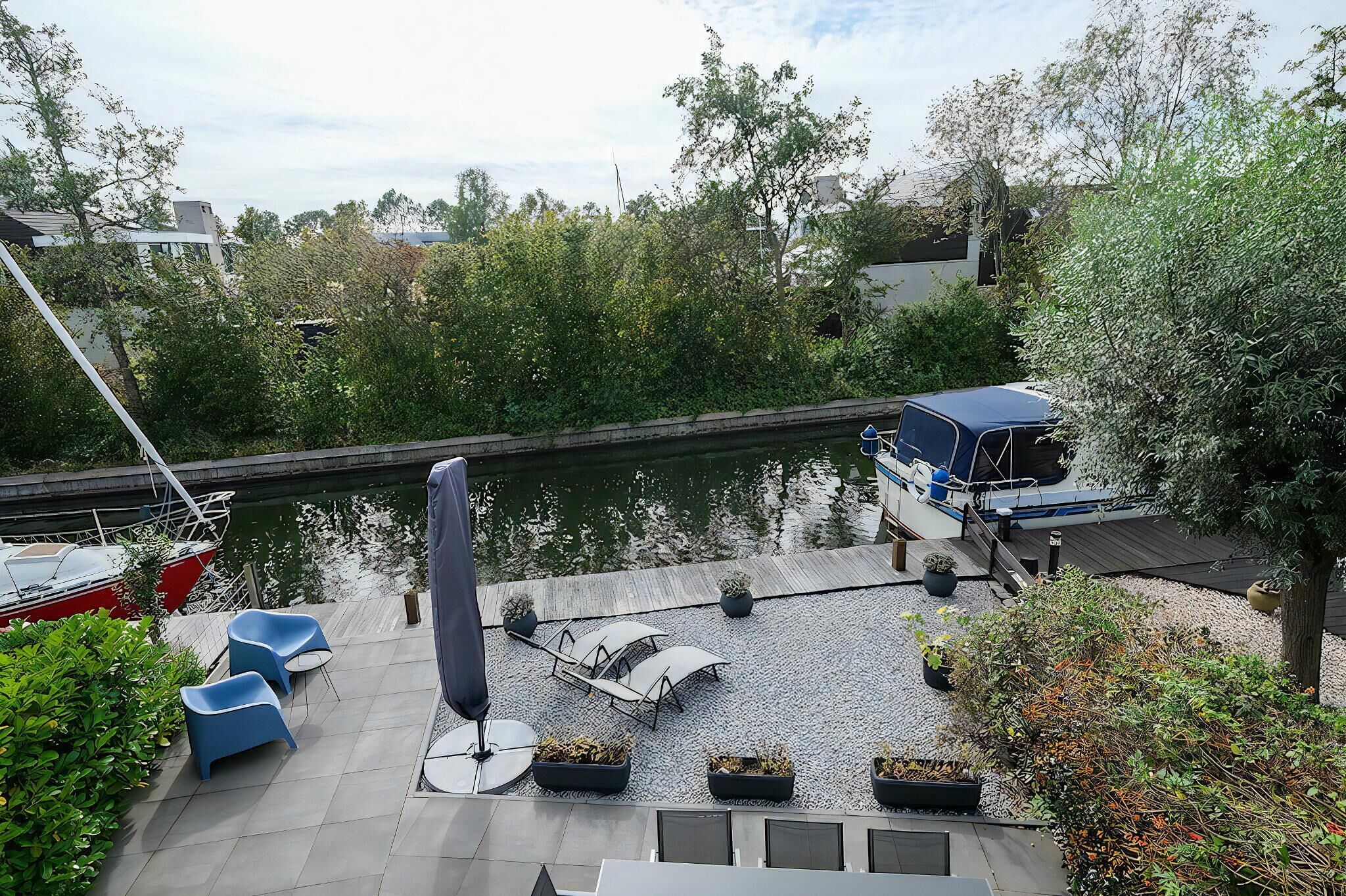 A riverside terrace with seating, a boat docked, and a calm water view.