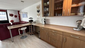 Une cuisine moderne avec des meubles en bois, un meuble à vin intégré et un coin bar rouge agrémenté de tabourets.