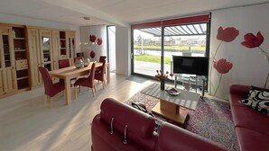 Un salon moderne comprenant un coin repas, un canapé, un téléviseur et une grande fenêtre donnant sur un parc.