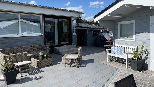 A modern outdoor patio area with a seating arrangement, a barbecue grill, and a covered outdoor kitchen.