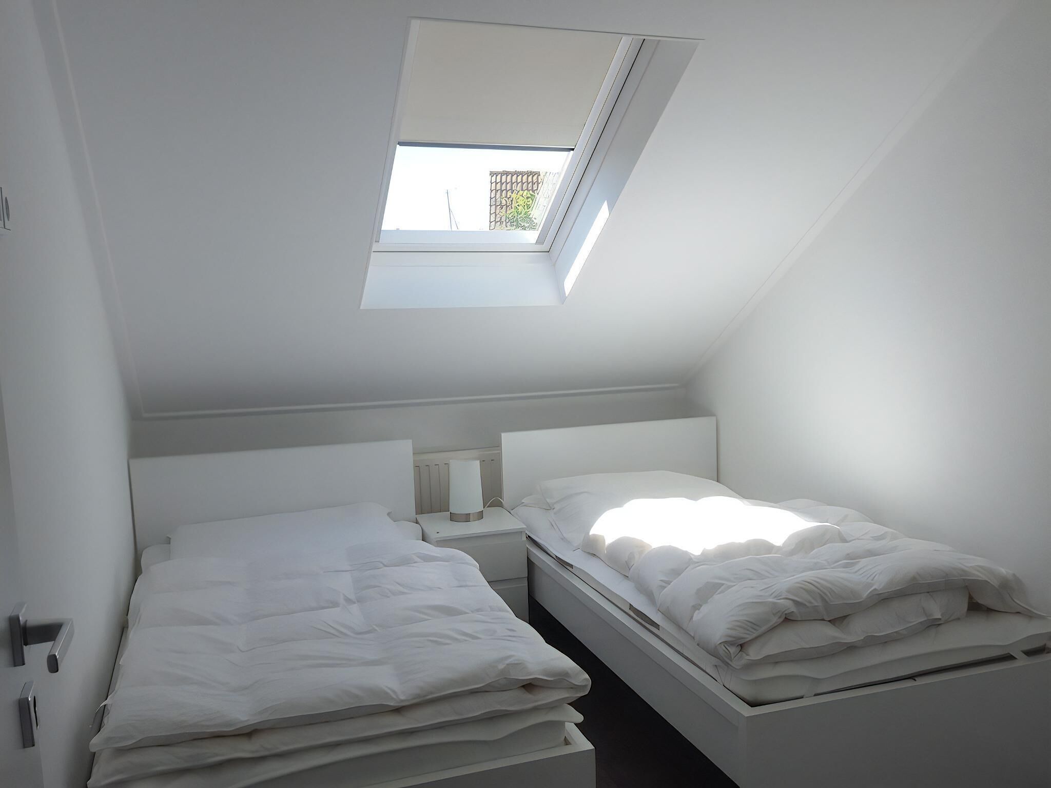 A small, modern bedroom with a skylight, a single bedside table, and a bed with white bedding.