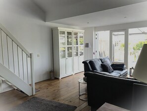 A modern living room with a black leather sofa, a white cabinet with glass doors, and a staircase. - Park De Markol River House (Lemmer)
