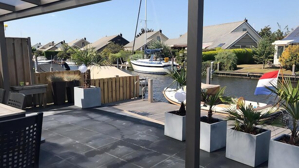 An outdoor patio with a view of a canal, boats, and houses. - Park De Markol River House (Lemmer)