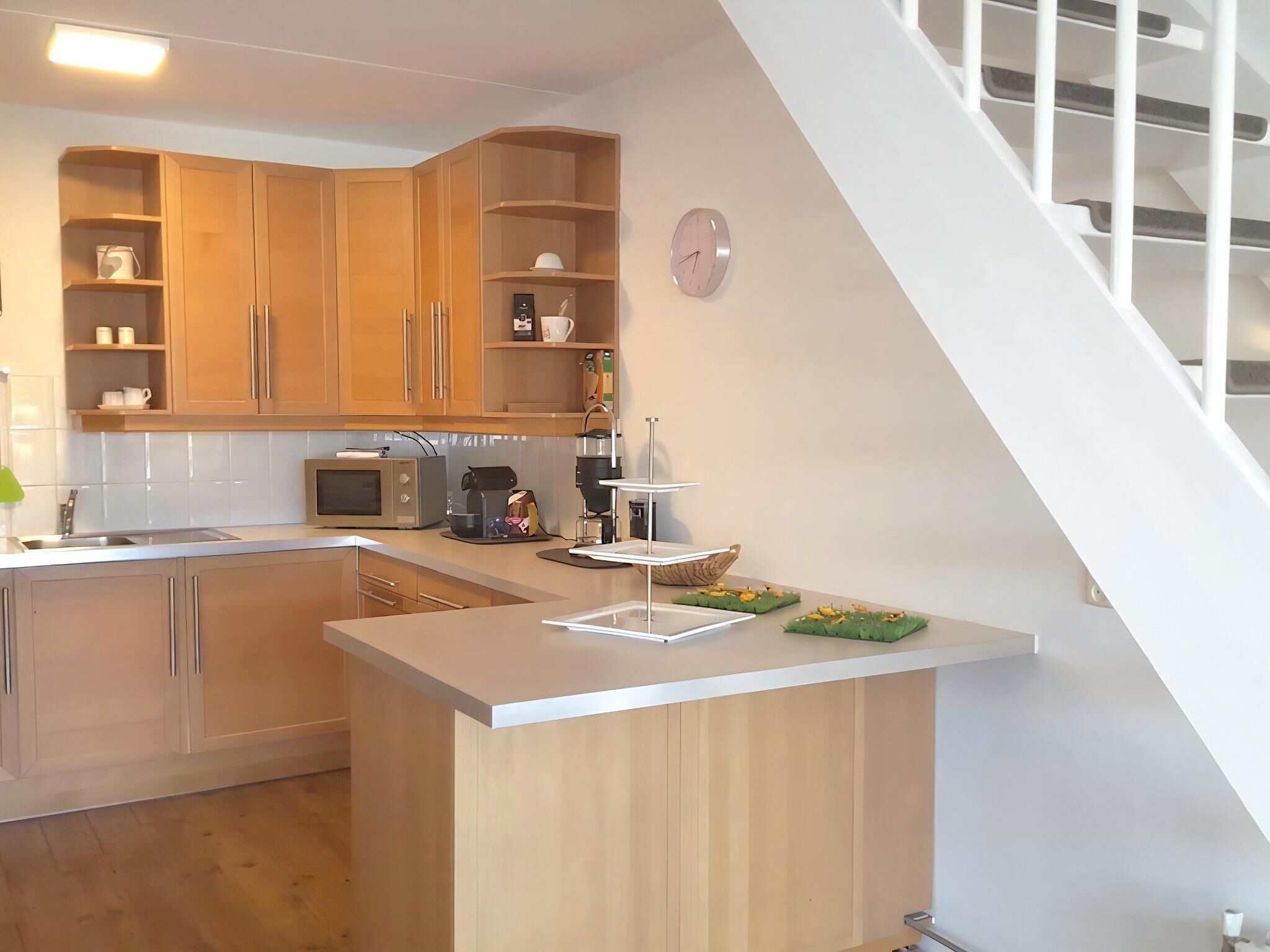 Une cuisine moderne avec des meubles en bois, un four à micro-ondes, une machine à café et une horloge au mur.