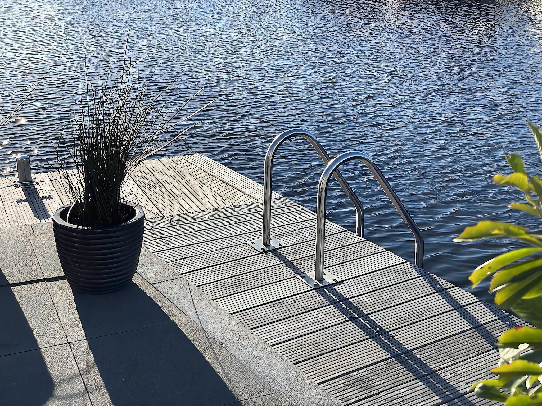 Un muelle de madera con barandillas metálicas y una planta en maceta.