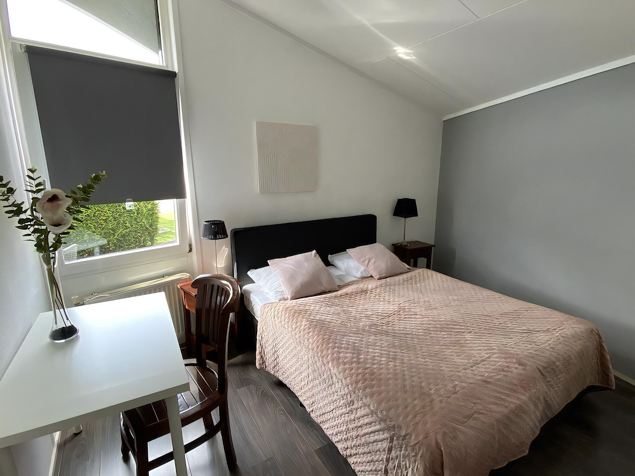 A bedroom with a bed, a desk, a chair, a window, and a lamp.