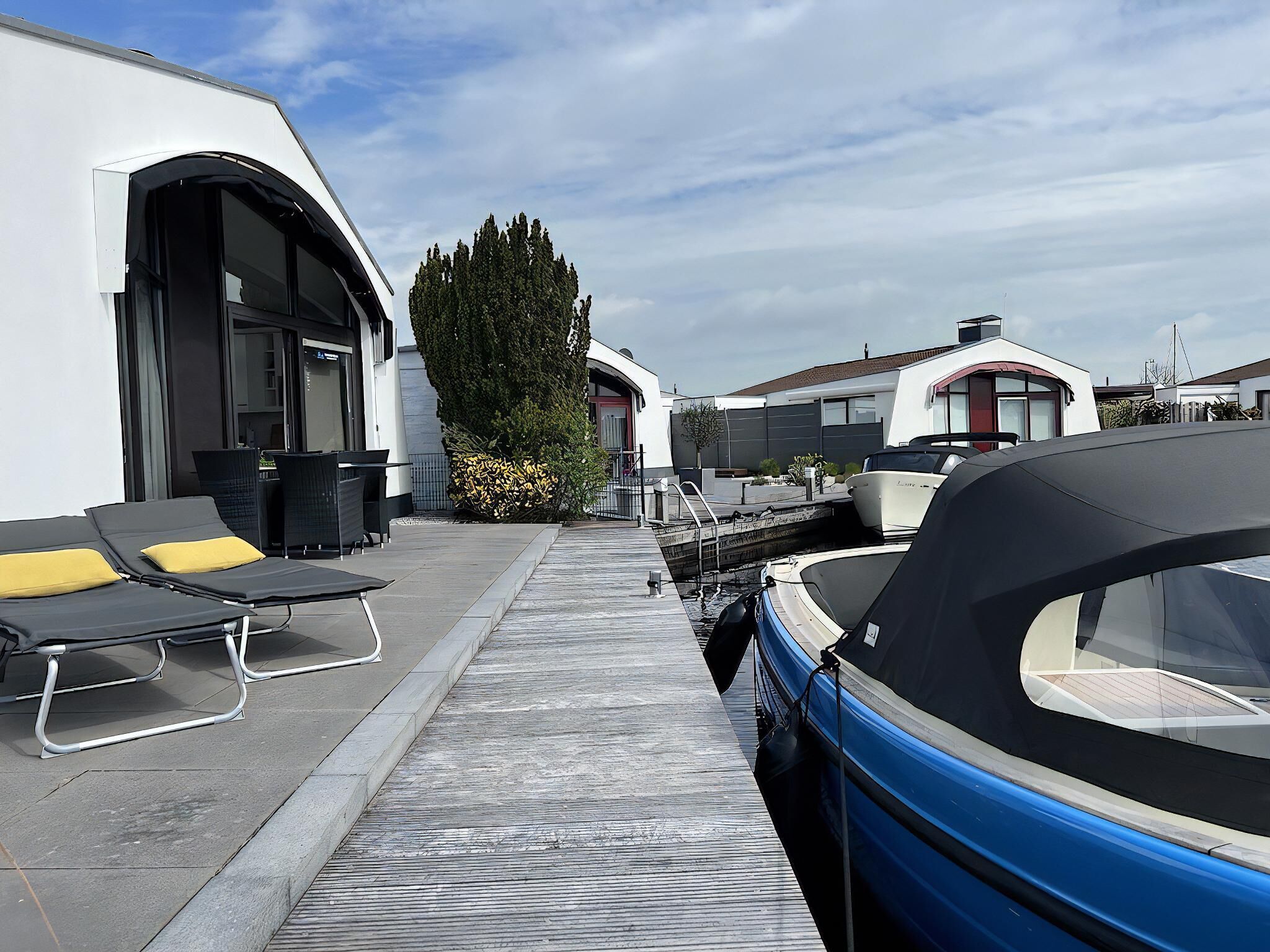 Un puerto deportivo con barcos amarrados, un paseo techado y mobiliario exterior con cojines amarillos.