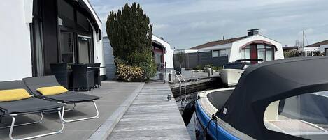 Un puerto deportivo con barcos amarrados, un paseo techado y mobiliario exterior con cojines amarillos.
