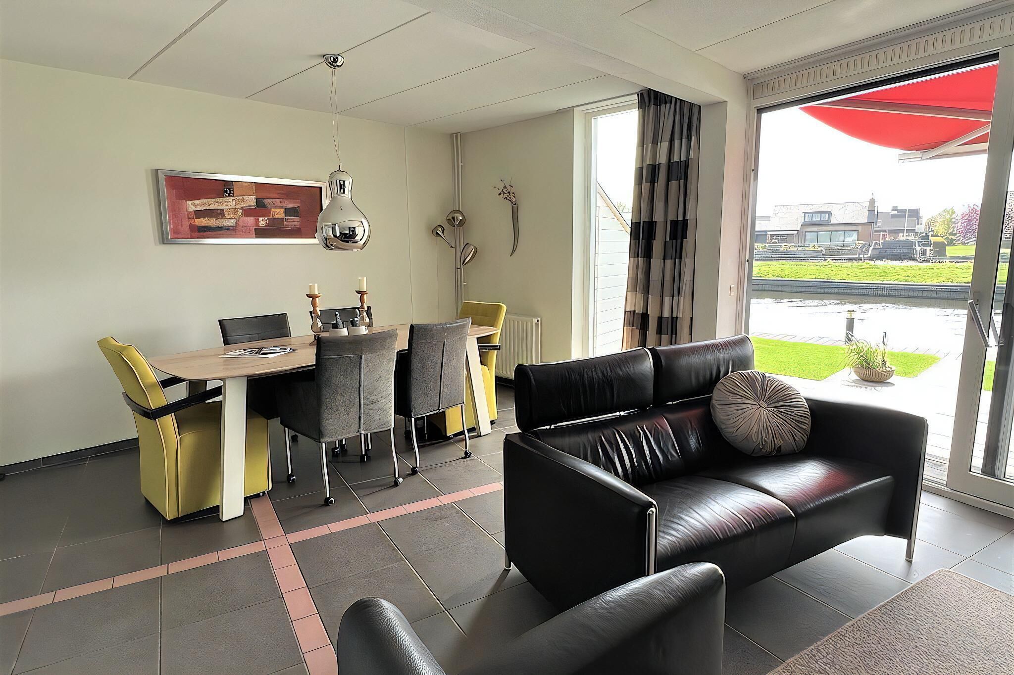 En moderne stue med en sort lædersofa, et spisebord med stole og et stort vindue med udsigt over et grønt landskab.