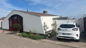 Un bâtiment blanc avec une porte rouge, une voiture garée devant, et un ciel bleu dégagé.