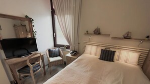 Une chambre d’hôtel comprenant un lit, un bureau avec une télévision, une chaise, une fenêtre avec des rideaux et une table de chevet avec une lampe.