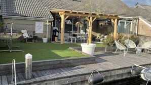 Une maison dotée d’un patio, d’un petit jardin et d’une jetée qui s’avance sur un plan d’eau.