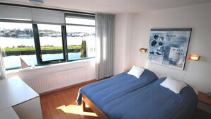 Et hotelværelse med en seng, et skrivebord, et vindue med udsigt over vand, og et kunstværk hængende på væggen.
