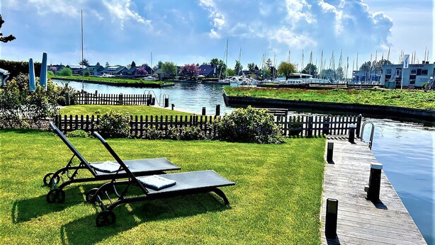 En græsplæne med en liggestol, en ankomstbro og en kanal med både i baggrunden.