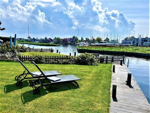 A grassy area with a lounge chair, a dock, and a canal with boats in the background. - Park Brekkense Wiel 127 (Lemmer)