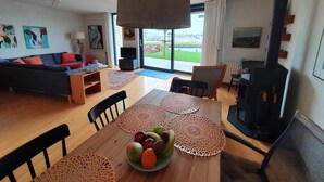En moderne stue med sofa, spisebord med frugt, pejs og stort vindue med udsigt.
