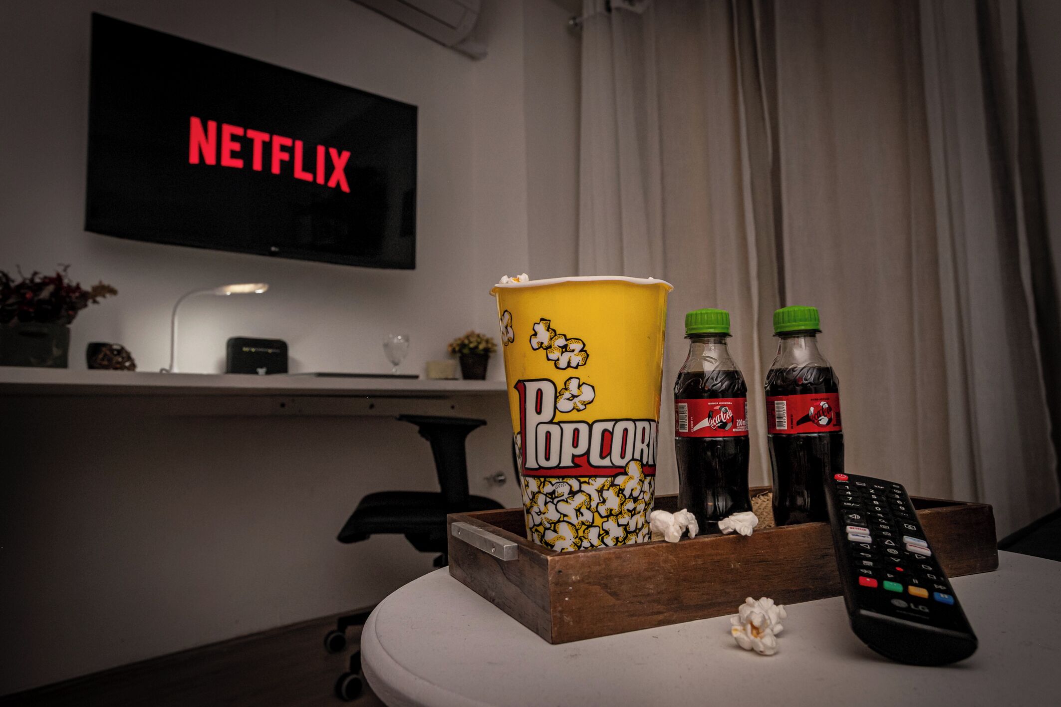 A television displaying 'NETFLIX,' popcorn, soda bottles, and a remote control on a table.