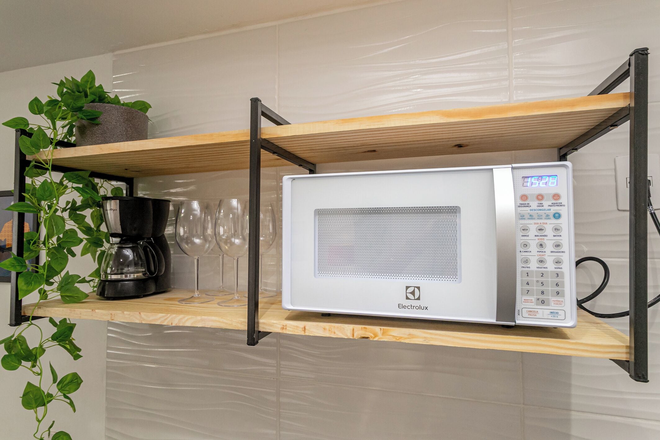 A kitchen with a microwave, a coffee maker, and wine glasses on a wooden shelf.