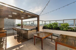 Un patio al aire libre con mesa y sillas de madera, una zona de bar y vistas a la ciudad.