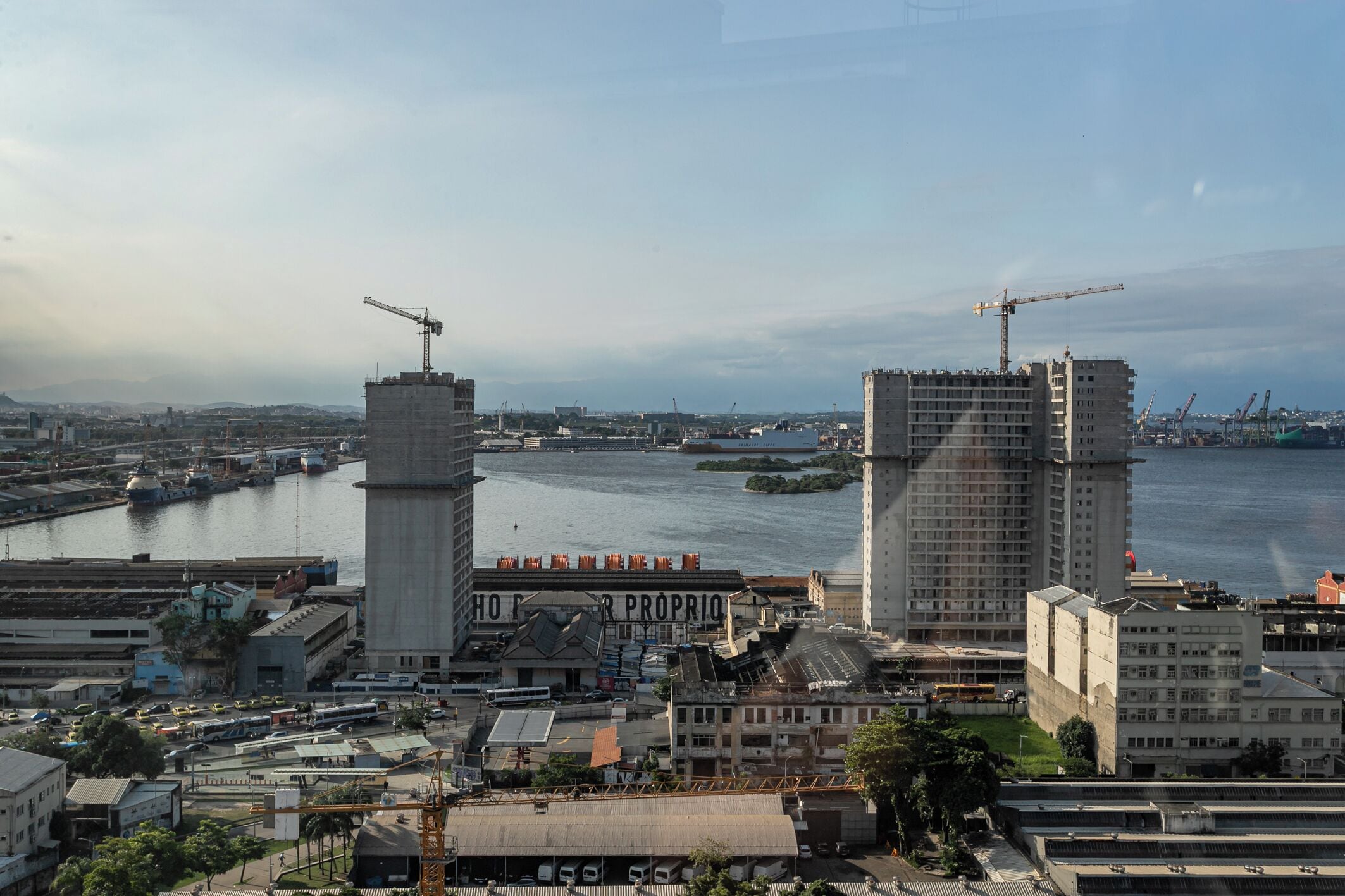 Un paysage urbain côtier avec un grand bâtiment en construction, une rivière et un pont.