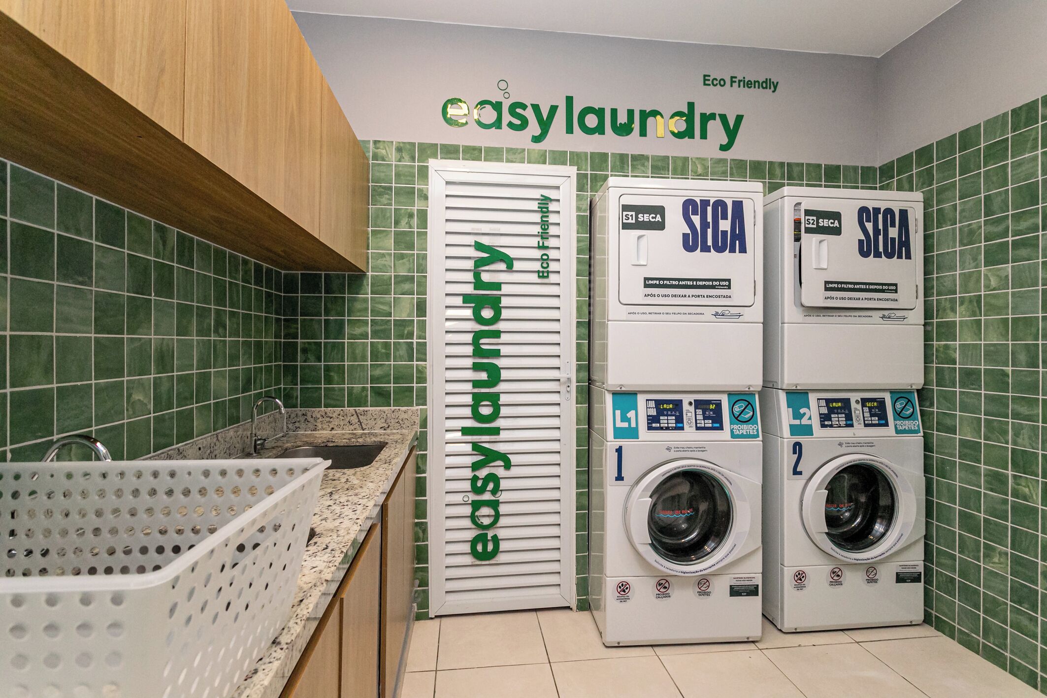A laundry facility with two SECA washing machines, a basket, and a sign indicating it's eco-friendly.