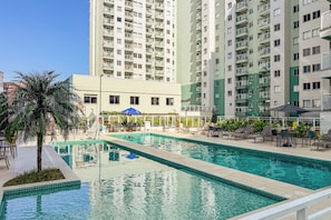 Piscina com espreguiçadeiras e guarda-sóis, cercada por edifícios residenciais altos.