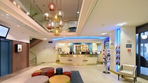 A modern hotel lobby with a reception desk, colorful seating, and a staircase. - Astra Studio (Vevey)