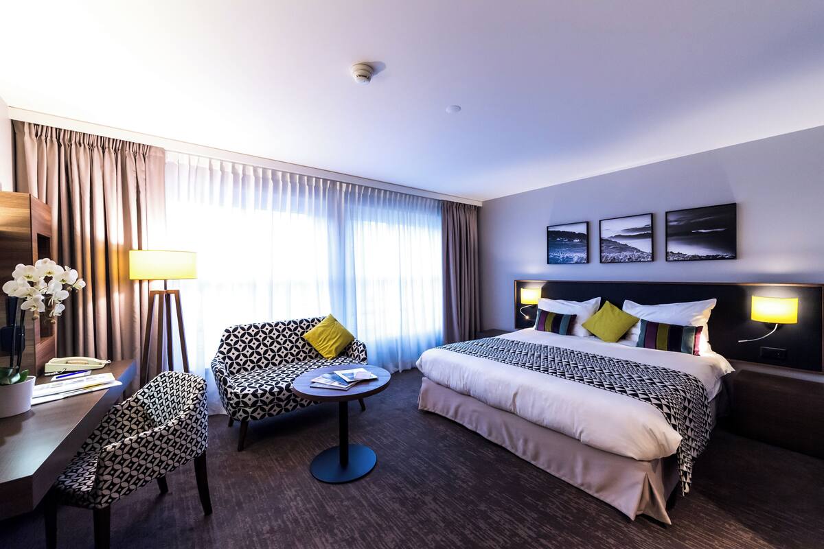 Una habitación de hotel con una cama, un escritorio con lámpara, una silla y una mesita.