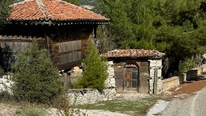 A rustic wooden building with a tiled roof, surrounded by trees and a gravel path. - Ali Paşa Konağı (Akseki)