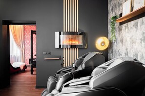 Quarto moderno com cadeira de massagem, lareira e prateleira na parede com uma planta.