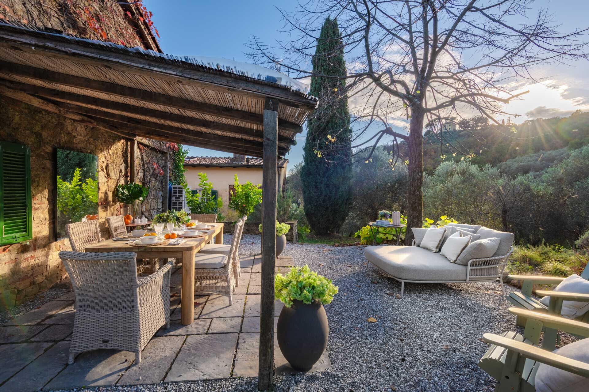 Eine rustikale Terrasse im Freien mit einem Esstisch, Korbstühlen, einem weißen Sofa und einem großen Blumentopf.
