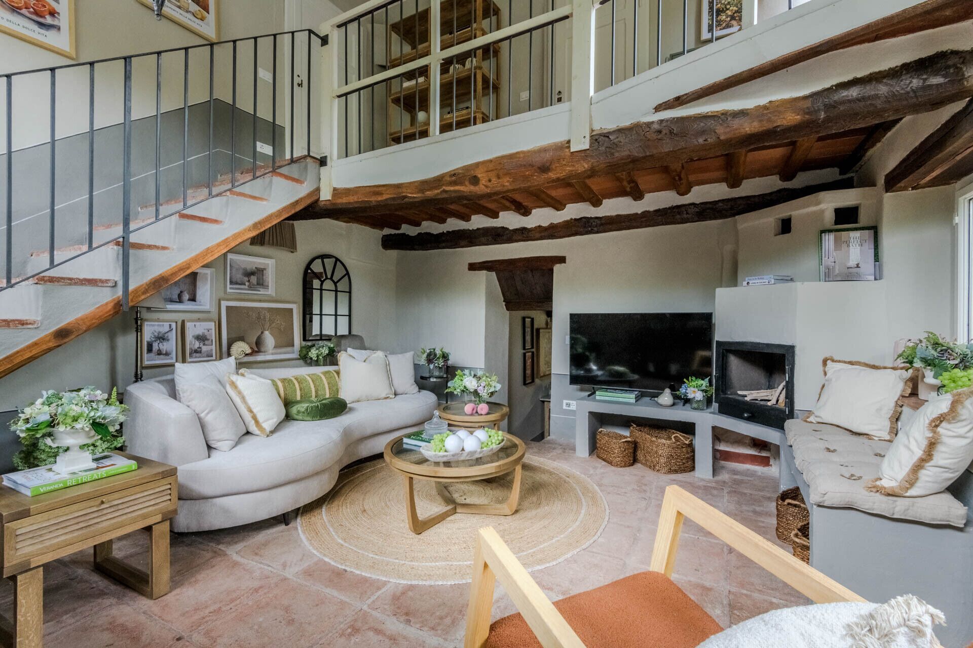 A spacious living area with a high ceiling, a staircase, a fireplace, and a television.