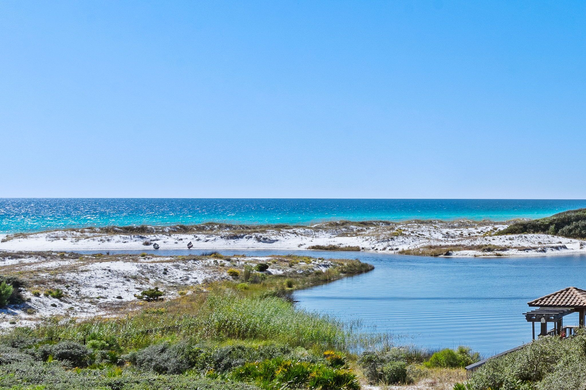 A coastal landscape with a clear sky, a body of water, and a small structure with a tiled roof.