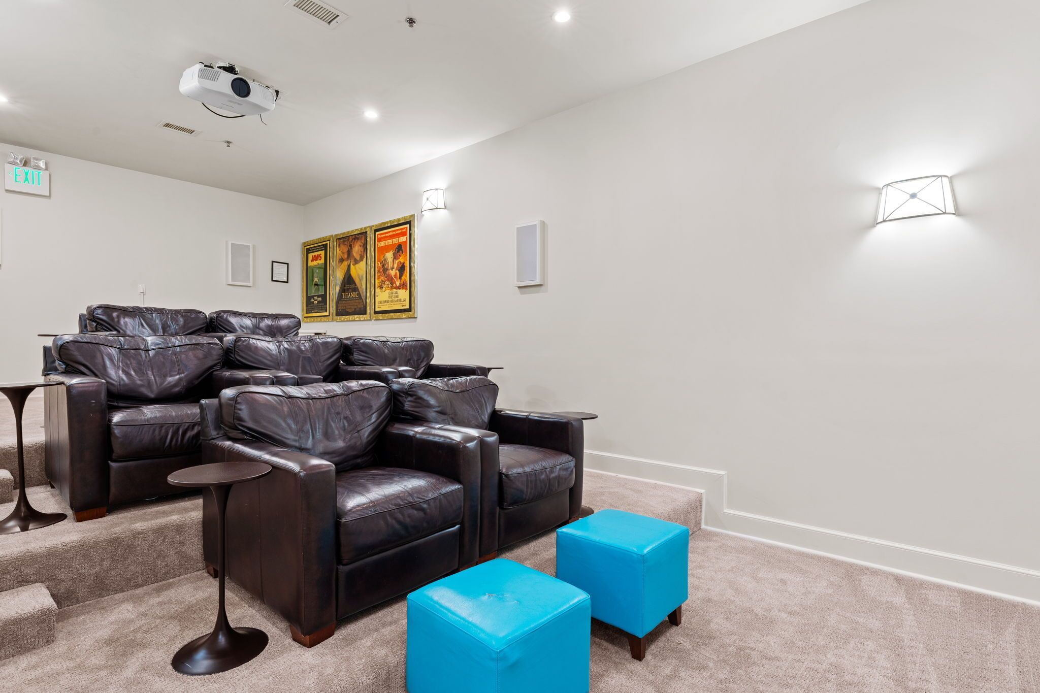 A room with a reclining leather sofa, a small table, and two blue ottomans.