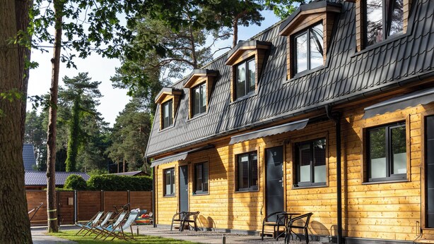 Eine Holzhütte mit geneigtem Dach, mehreren Fenstern und einer Terrasse mit Sitzgelegenheiten.