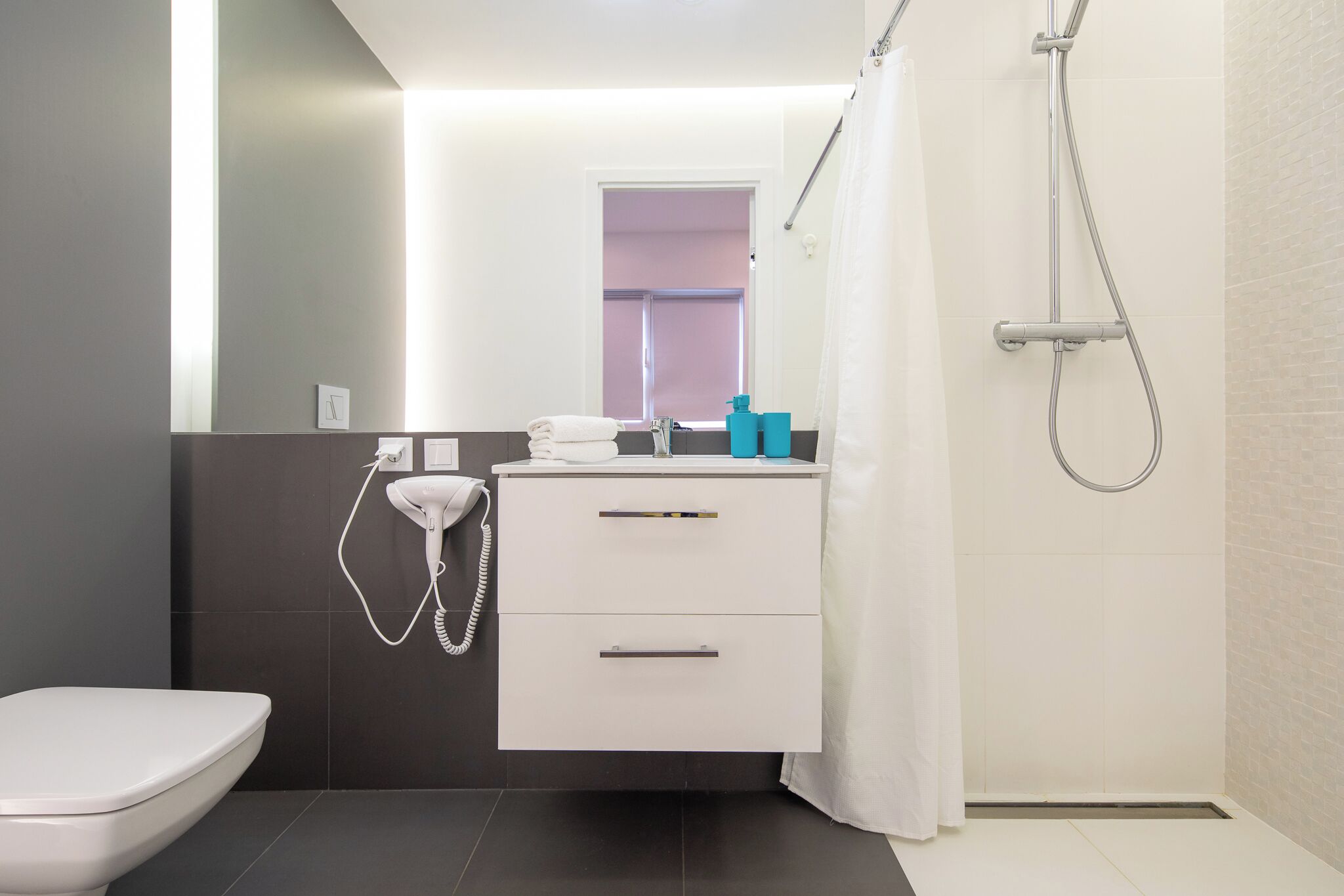 A modern bathroom with a toilet, a sink with a mirror, a shower, and a towel rack.